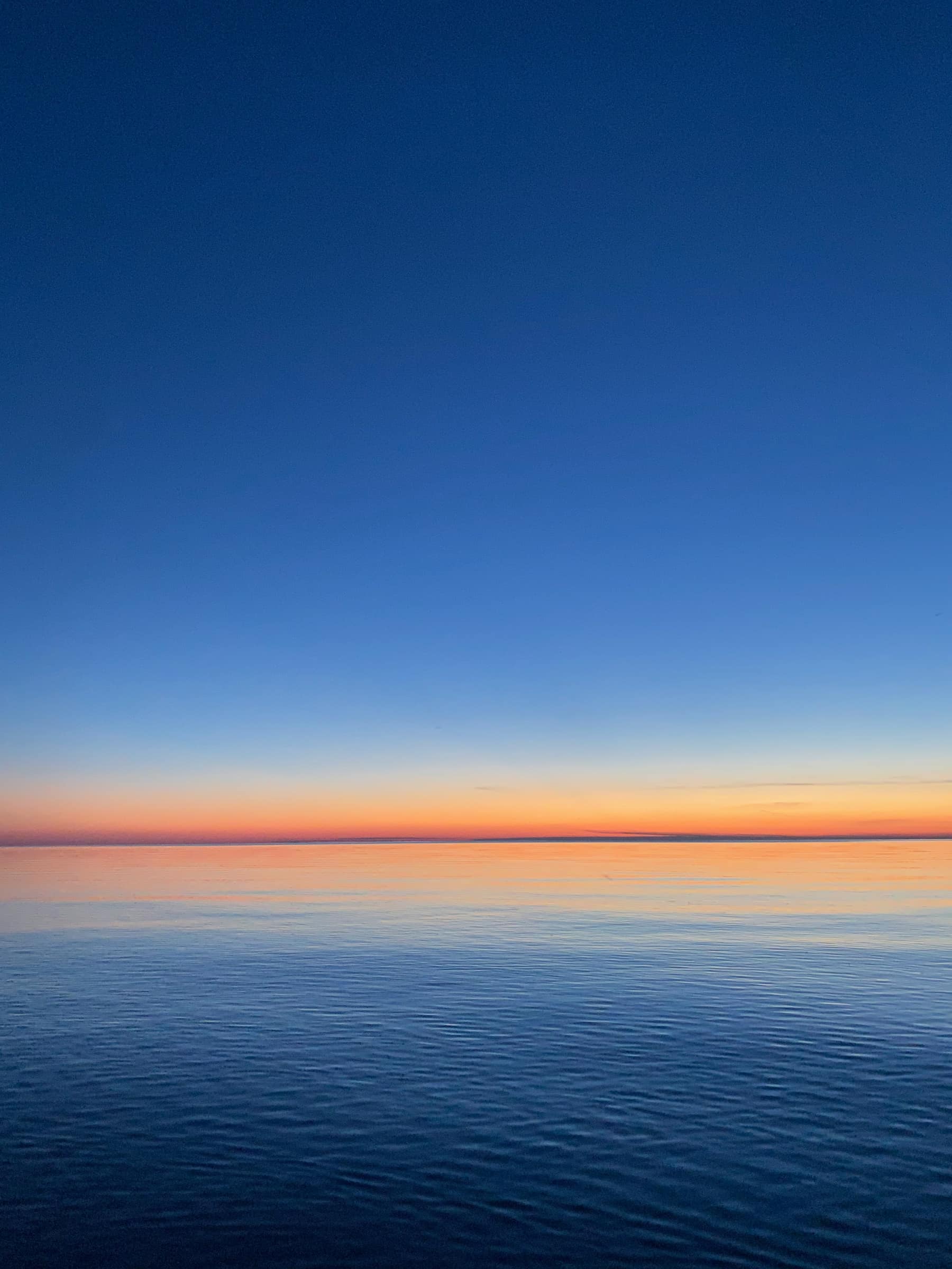 Calm ocean horizon at dusk fading from deep blue to amber